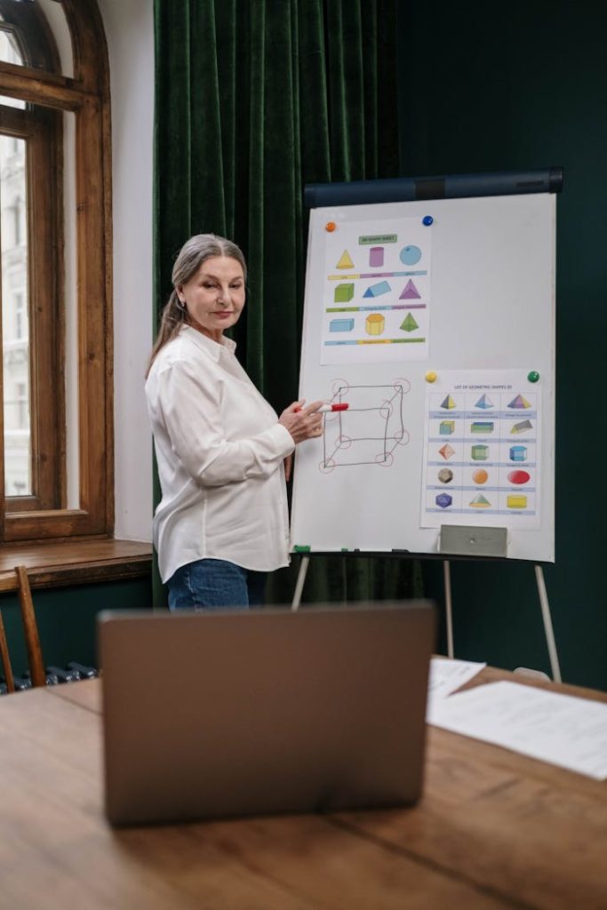 Senior woman teaching geometry concepts online with laptop and whiteboard.